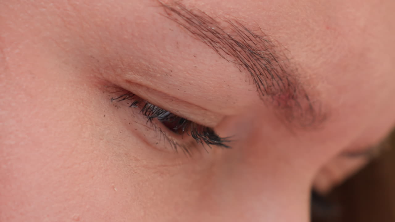 극단적인 클로즈업으로 사람 얼굴의 디테일에 초점을 맞추고, 눈꺼풀은 내려가 있고 긴 속눈썹이 드리워져 있으며, 눈썹과 피부 질감이 선명하고, 조용히 집중하는 사람의 모습, 시선은 아래로 향하고 있어요.