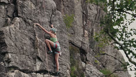 young woman with helmet and ropes climbing cliff, side view