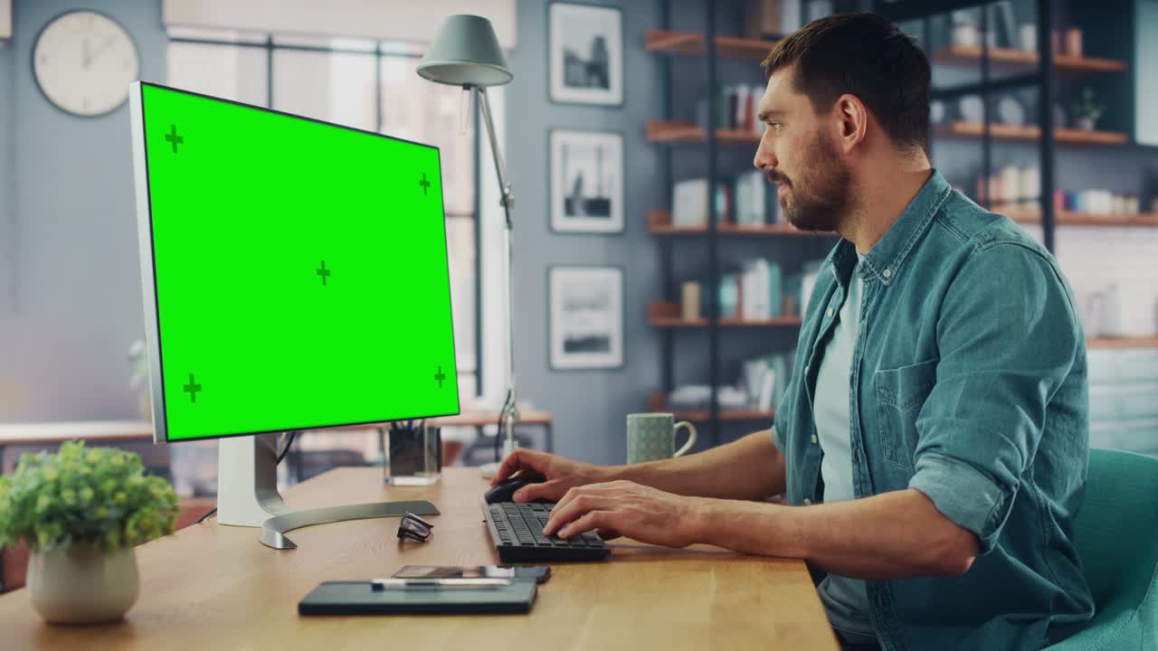 Handsome Caucasian Specialist Working on Desktop Computer with Green Screen Mock Up Display at Home Living Room. Happy Freelance Man Smiles to the Camera and Shows a Thumbs Up Hand Gesture.