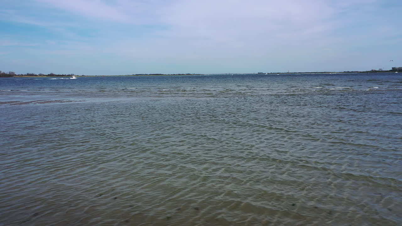 낮은 각도의 드론이 해변을 가로질러 물을 바라보며 수평선을 바라보고 있습니다.