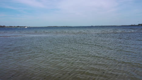 A-low-angle-drone-shot-over-a-beach,-looking-out-at-the-water---the-horizon