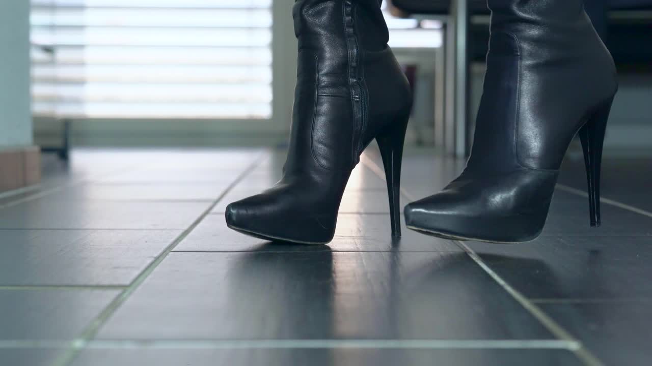 una chica baila con sus sexys botas negras de tacón de aguja delante de la cámara