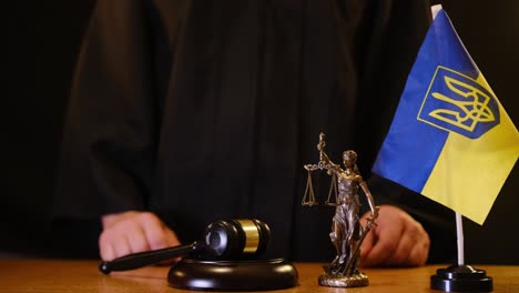 a judges gavel lying beside the statue of justice, along with the ukrainian flag, symbolizing law and order in society