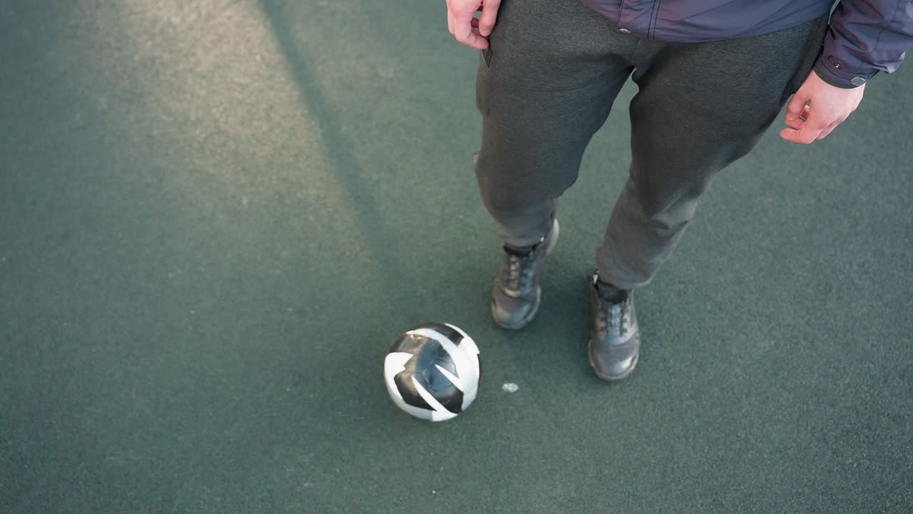 vista aérea de un atleta que demuestra movimientos precisos del tobillo con una pelota de fútbol en el suelo, centrándose en la agilidad y el control durante una sesión de entrenamiento en una superficie deportiva texturizada en un entorno al aire libre
