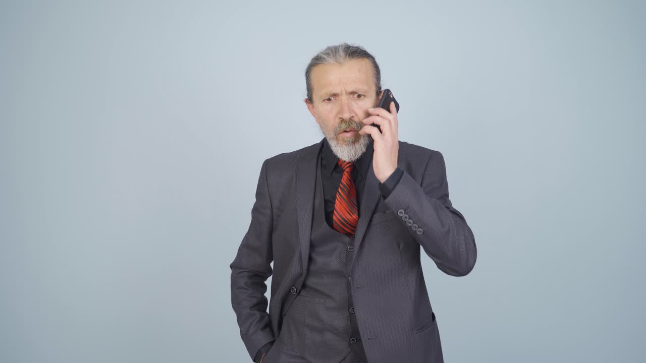 사업가가 전화로 이야기하는 동안 방해받고 화를 내고 있습니다.