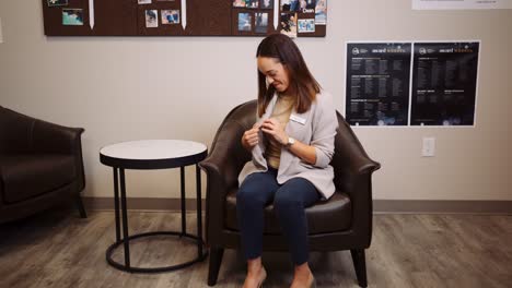 A-Young-Professional-Business-Woman-Sits-in-Leather-Chair-inside-Retail-Furniture-Clothing-Store-Office-Breakroom-Takes-Off-Radio-Walkie-Talkie-Communication-System-Clocking-Out-Waves-Goodbye-Coworker