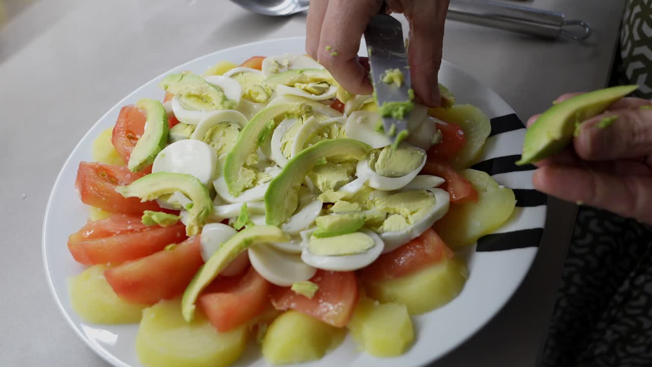 Primo piano di mani che preparano un'insalata fresca con avocado, pomodoro, patata e uovo