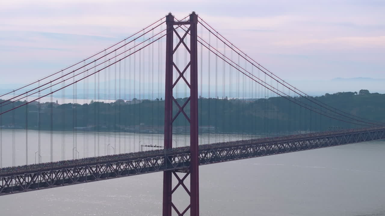 Half marathon and 10K long distance running event in Lisbon, Portugal, Europe. Runners crossing the iconic famous red 25th April suspension bridge. Professional sports aerial drone shot