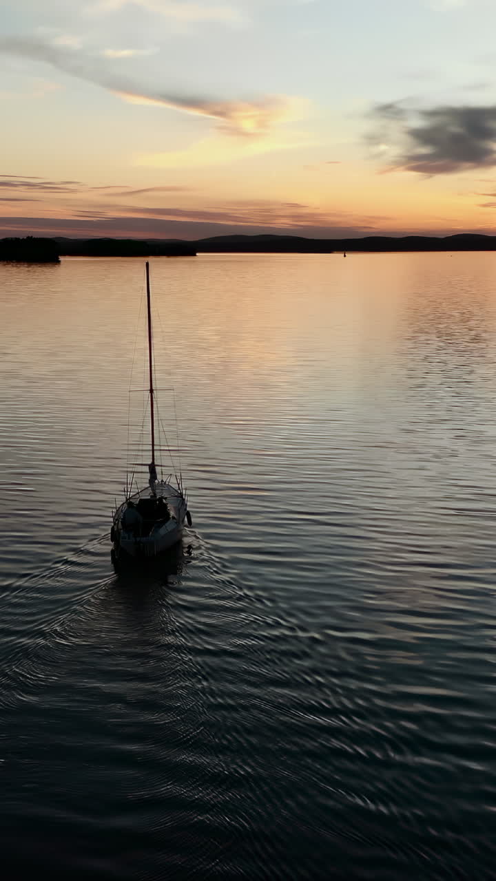 Vista aerea di una barca a vela solitaria che naviga dolcemente su un lago tranquillo durante un tramonto colorato.