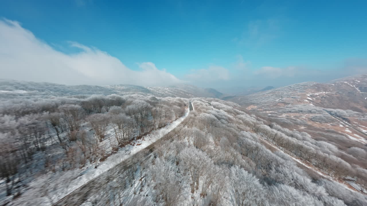 Aerial FPV drone view of snowy mountains and winding road under a blue sky