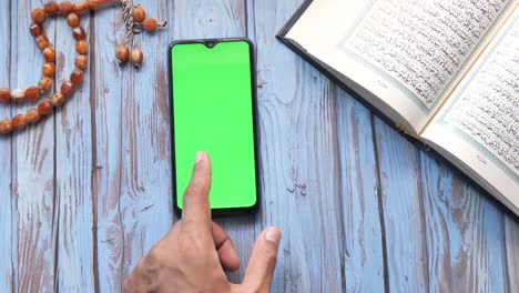 muslim person using smartphone with quran and rosary