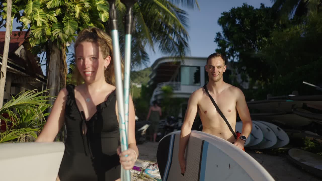 Couple walking on a tropical beach with paddleboards