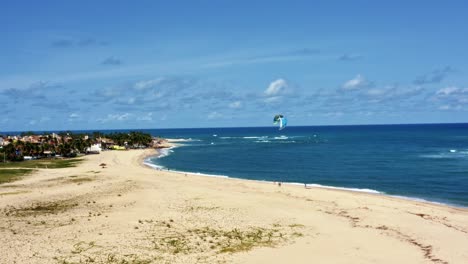 Dolly-out-aerial-drone-shot-of-kite-surfers-pratciting-on-the-tropical-Barra-do-Cunhaú-beach-in-Canguaretama-where-the-large-Curimataú-river-meets-the-sea-in-the-state-of-Rio-Grande-do-Norte,-Brazil