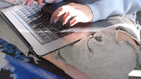 mujer con uñas largas manicura escribiendo un dispositivo portátil moderno con palabras clave sentado con las piernas cruzadas usando jeans rasgados de moda, investigación de navegación por internet conexión rápida 5g, manos femeninas cierran en cámara lenta