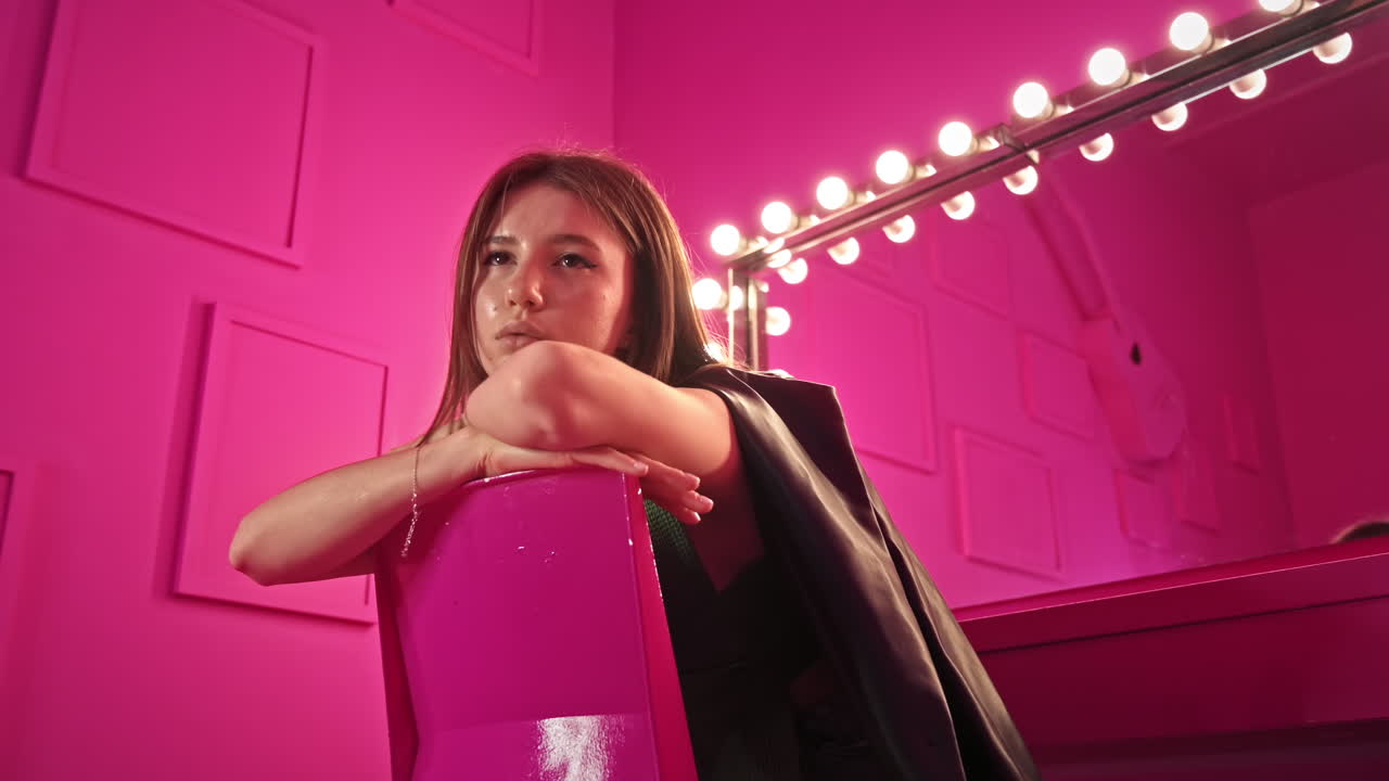 Giovane donna che posa in uno studio con pareti e mobili rosa. Specchio con lampade