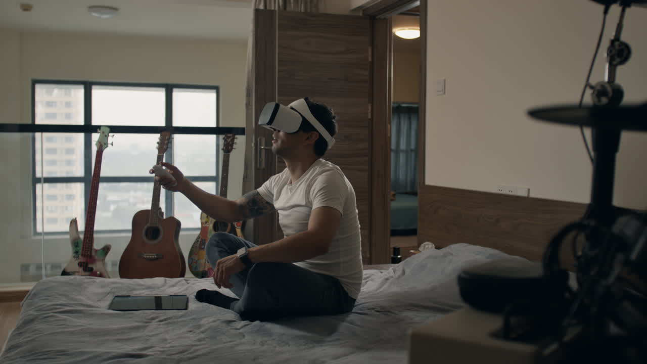 Man using VR headset gestures mid-air while sitting on bed in apartment music studio