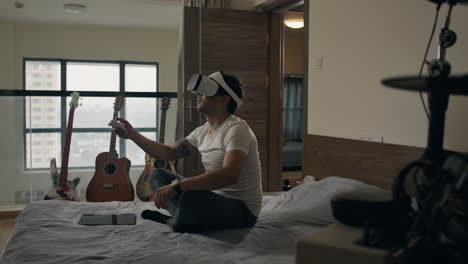 man using vr headset gestures mid-air while sitting on bed in apartment music studio
