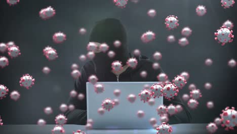 Animation-of-of-macro-covid19-cells-over-man-wearing-balaclava,-using-a-laptop