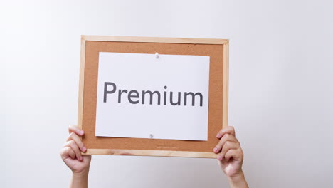 woman's hand shows the paper on board with the word premium in white studio background with copy space