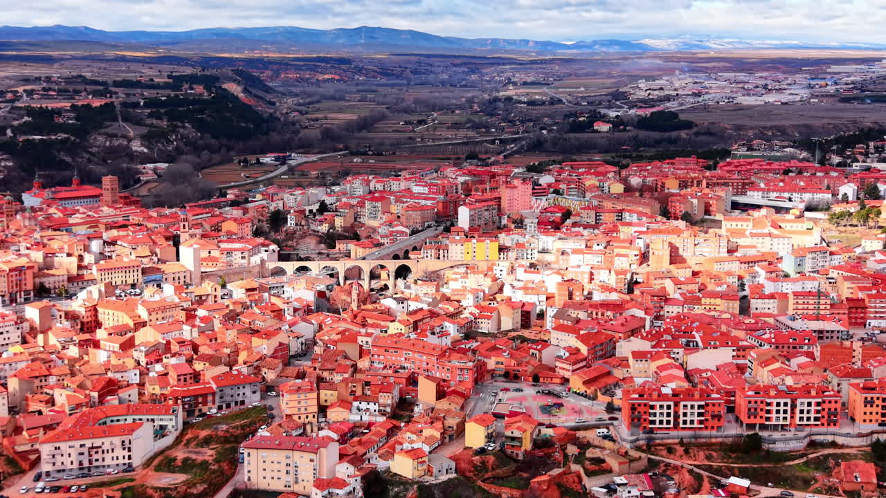 Luftfoto af tætpakkede boligbygninger med røde tegltage og en stenbueviadukt i centrum. Bylandskab i Teruel, Spanien