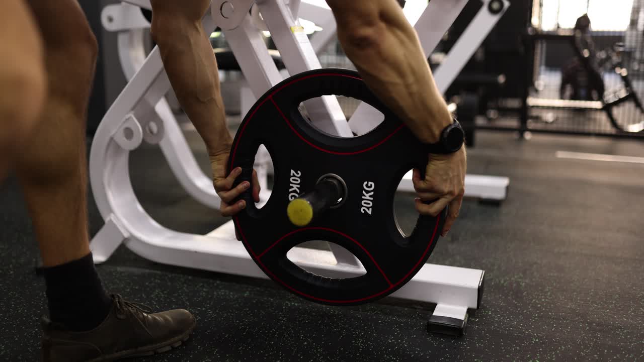 A person loading a 20kg weight plate onto gym equipment
