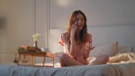 adolescente relajado hablando teléfono inteligente en la cama. chica sonriente descansando dormitorio acogedor