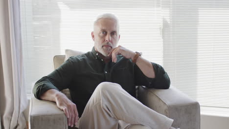 retrato de un hombre caucásico de mediana edad sentado en un sillón en casa con espacio para copiar