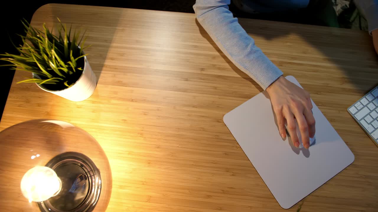 mujer trabajando en la computadora por la noche. vista de las manos de la mujer en cómoda ropa de casa sentada en un escritorio de madera iluminado por una lámpara y usando el ratón y el teclado de la computadora en una habitación oscura por la noche