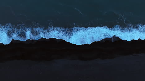 dark blue ocean waves splashing black sand beach, aerial top down shot