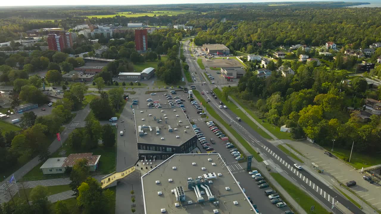 Aerial drone video orbiting and flying obove a small urban enironmental Tabasalu city where large modern shopping center and highway with cars visible and large blue ocean in the horizon, Baltics