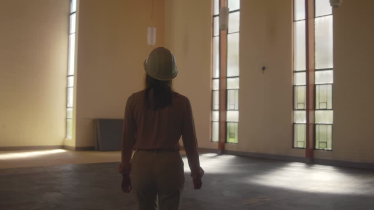 arquitecta caminando con un sombrero duro blanco entrando en una habitación enorme durante una observación