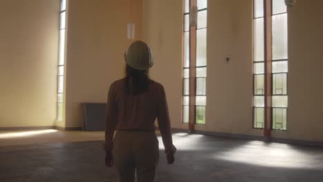 female architect walking with a white hard hat entering a huge room during an observation