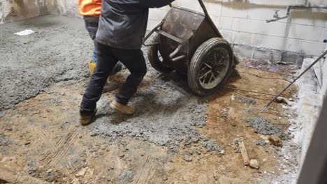 two people wheel barling cement into room to repair floor