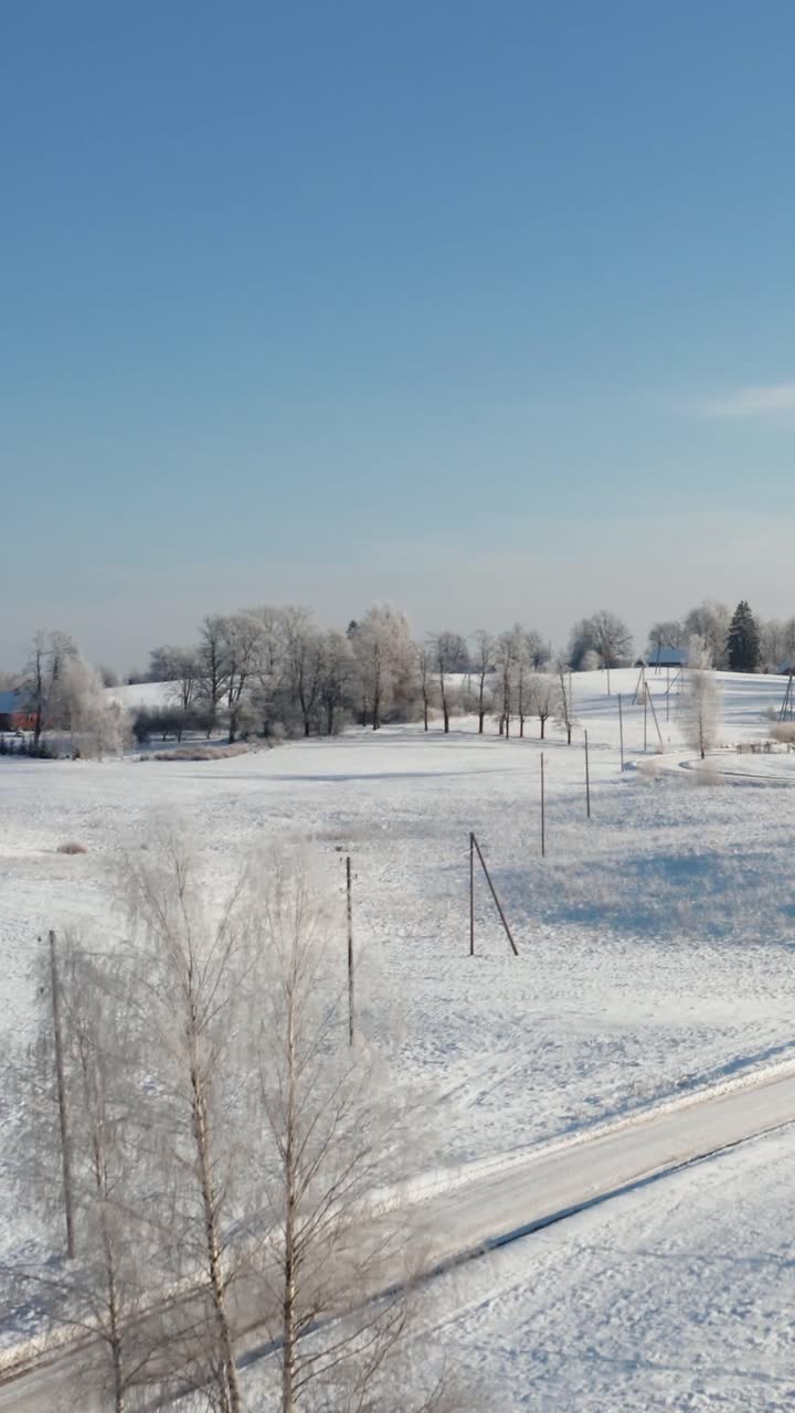 Vertical winter morning aerial drone view over the countryside with winding road and country houses over the landscape. Vast panoramic view of snow covered land and frost on the trees.