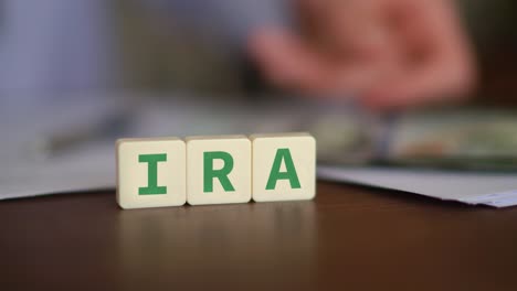 letter blocks forming ira with person counting money in defocused background