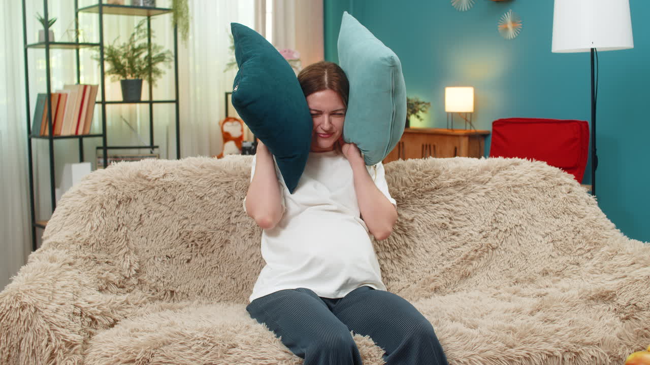 Pregnant woman tries relaxing but neighbors knock sofa shows stop gesture covers ears with pillows