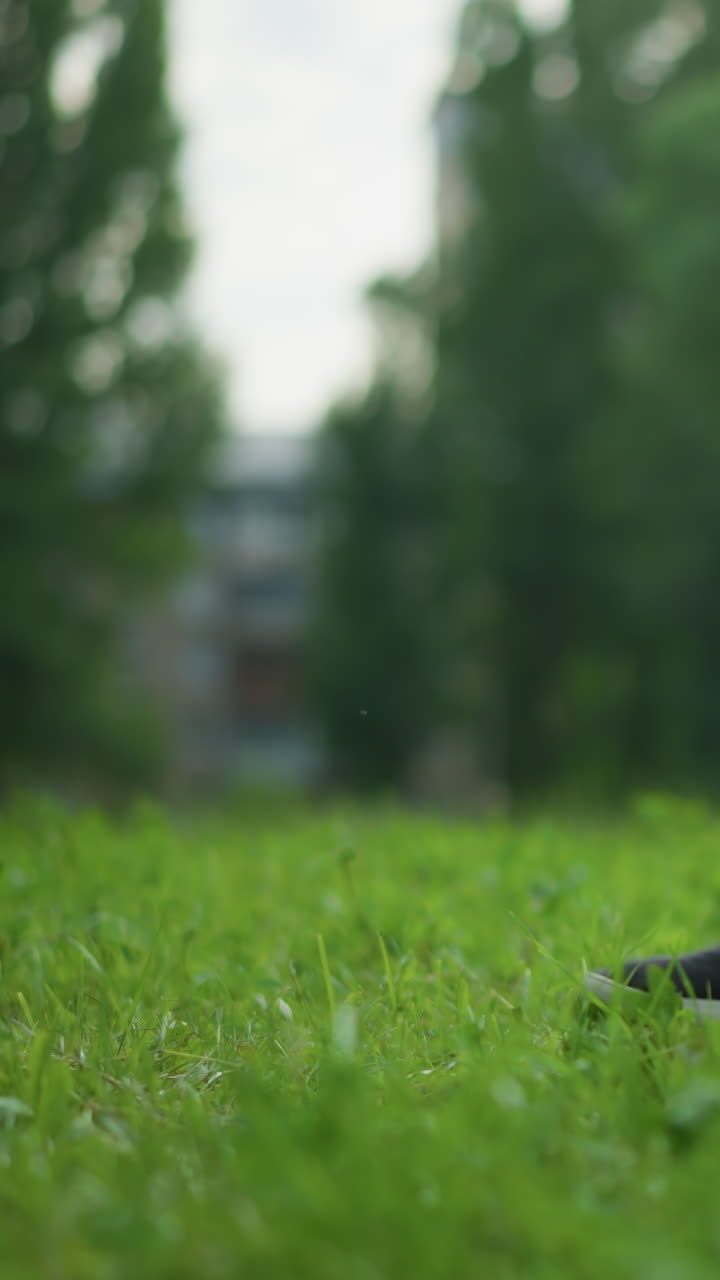 A close-up leg view of someone in gray shorts skillfully tapping a soccer ball on a lush, grassy field, with trees in the background