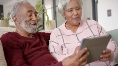 happy senior biracial couple using tablet for video call, unaltered, in slow motion