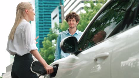 Progressive-businessman-and-businesswoman-use-charging-station-for-EV-car.