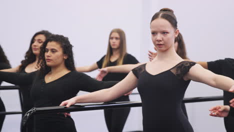 male and female students at performing arts school rehearsing ballet in dance studio using barre