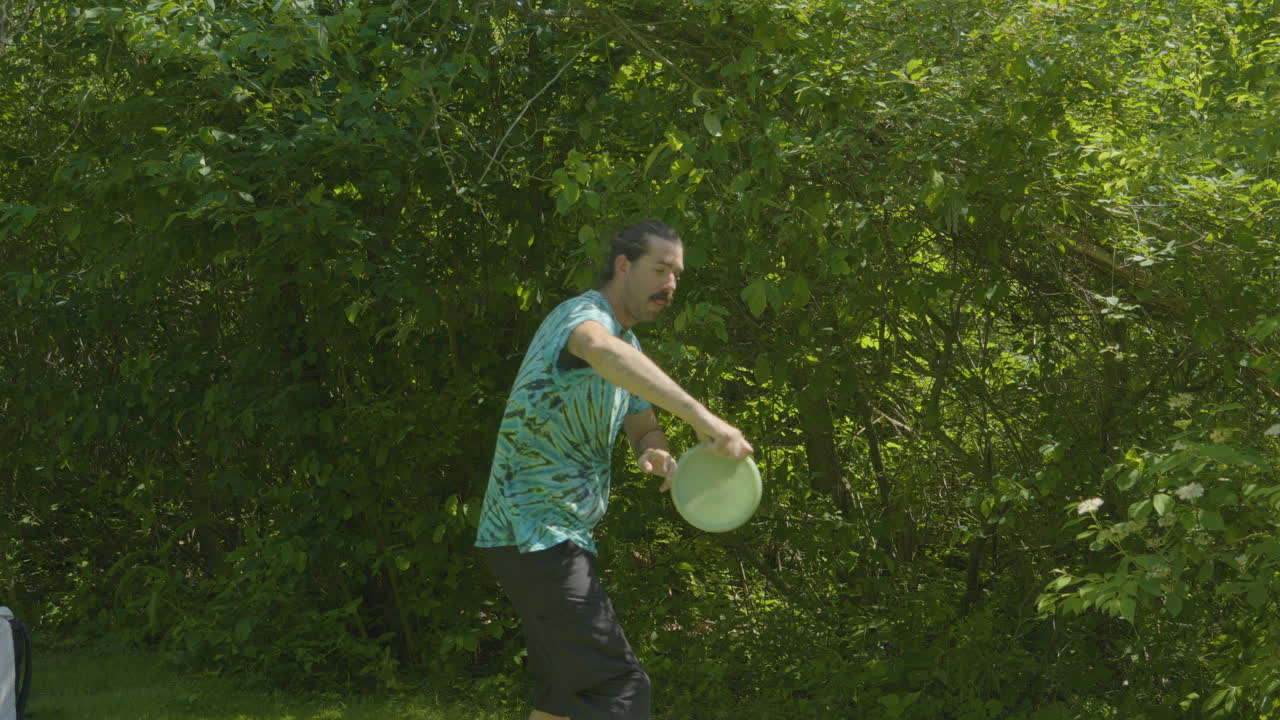 un hombre se prepara para lanzar un disco durante un juego de disc golf, con un denso follaje verde como telón de fondo