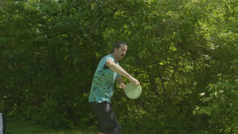 a man prepares to throw a disc during a disc golf game, with dense green foliage as his backdrop