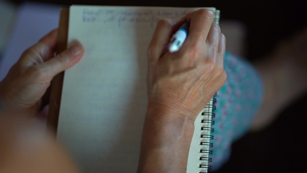 anciana escribiendo con su mano derecha en un cuaderno con un bolígrafo multicolor