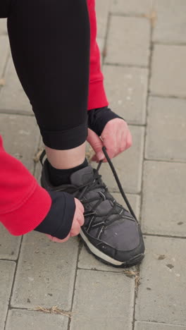 vista lateral de una atleta en cuclillas en un camino entrelazado atando su cordón derecho, enfoque de primer plano en las manos y el zapato, destacando la preparación y la dedicación para la actividad al aire libre en el fitness