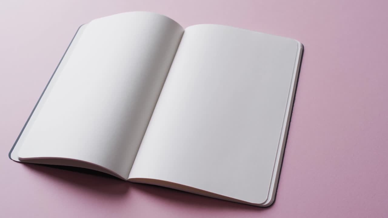 Close up of open blank book with copy space on pink background in slow motion