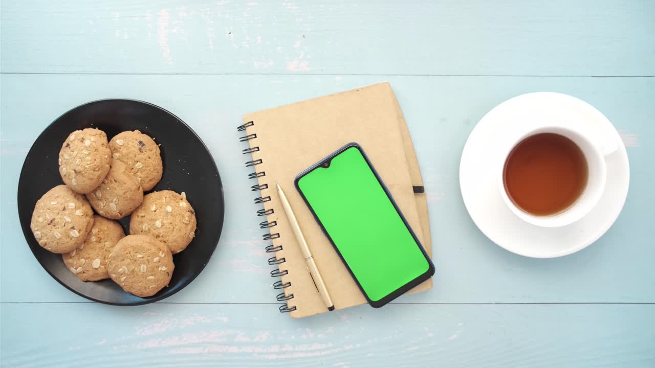 escena de desayuno simple con galletas, té, cuaderno y teléfono inteligente