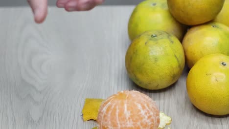 close-up of hands peeling oranges, revealing juicy segments on a wooden table.