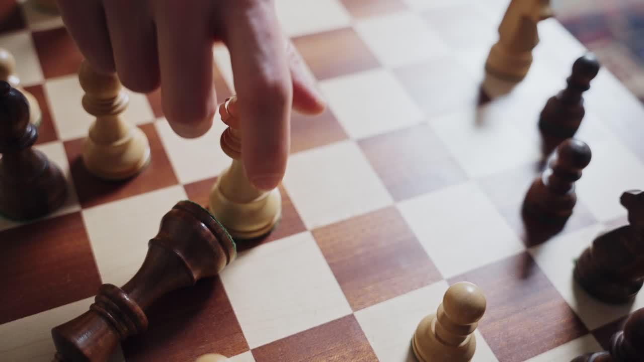 Chess board from above as hand uses white queen piece to topple black king in checkmate move. Power play and leadership action symbol. Strategic thinking and planning in business and politics