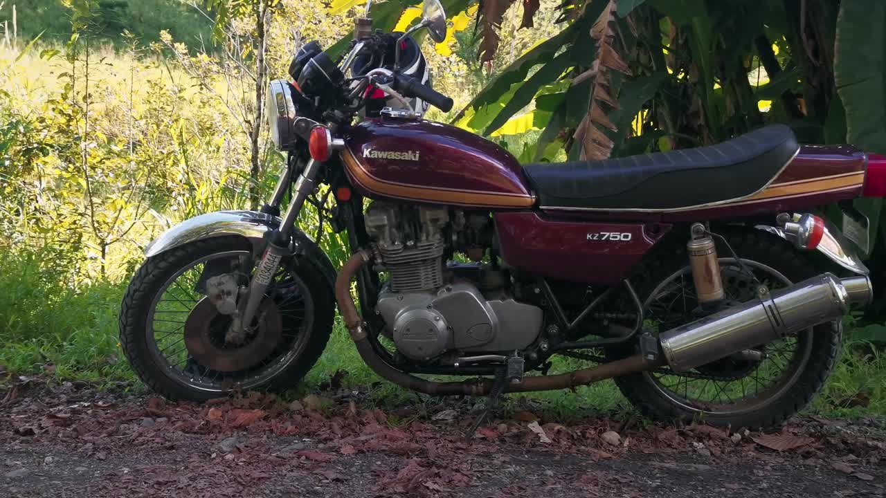 1976 Kawasaki KZ 750 motorcycle parked in the shade of a big palm tree in central America. Orbiting gimbal shot