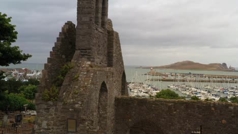 aerial slow motion dolly orbit around front entrance facade wall of broken brick ruins in abbey of howth, ireland's eye in backdrop